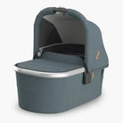 A stone blue bassinet with a sunshade, mesh panels, and a carry handle, designed for newborns.