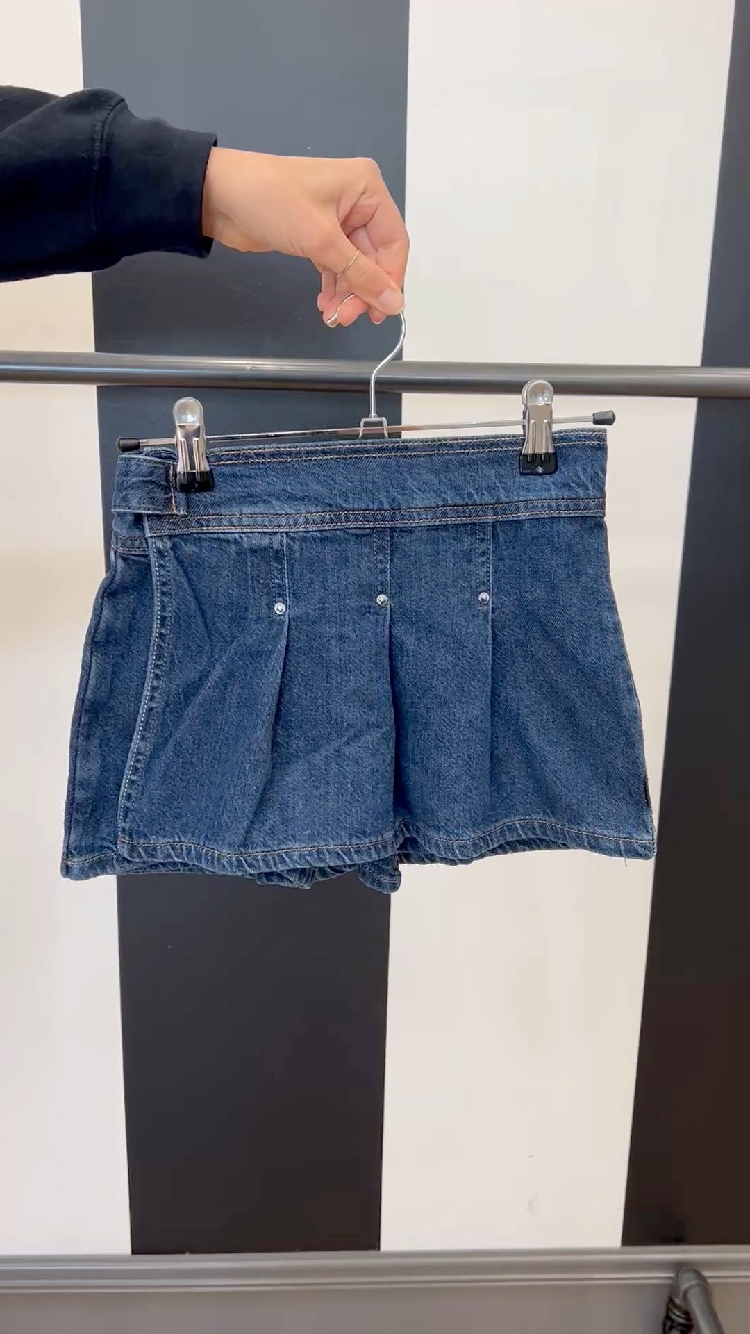 Blue denim shorts on a hanger against a black and white striped background