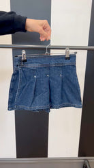 Blue denim shorts on a hanger against a black and white striped background