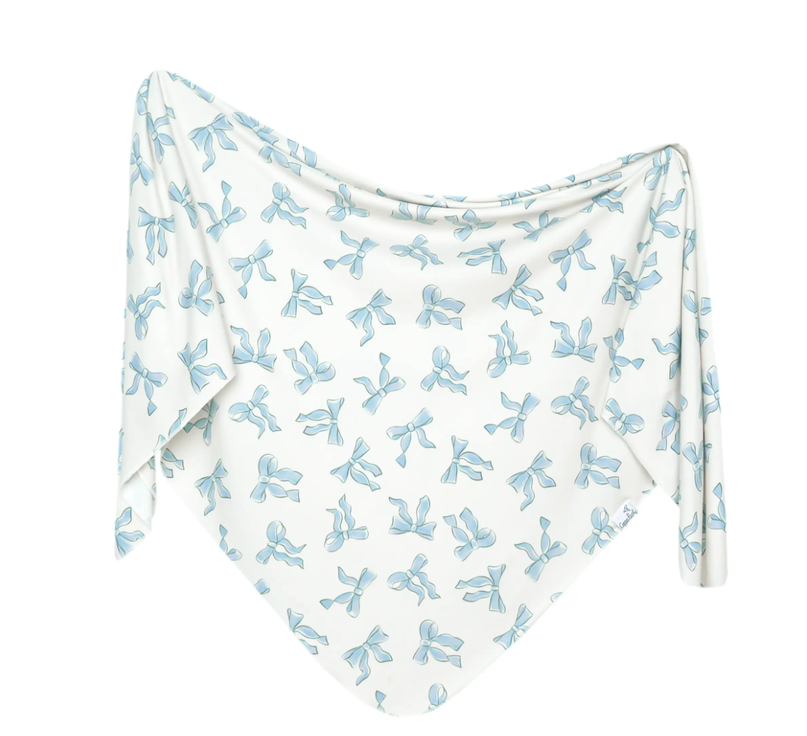 A white knit swaddle blanket with a blue bow pattern, displayed on a flat surface.