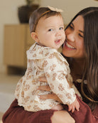 Woman holding a baby wearing a floral outfit indoors