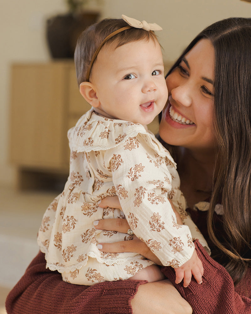 Woman holding a baby wearing a floral outfit indoors