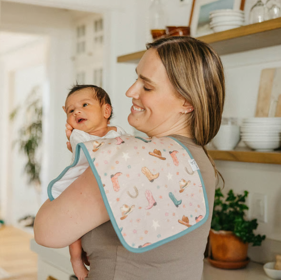 woman holding infant smiling with cowgirl boot print burp cloth